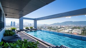 A rooftop infinity pool with a city view, lounge chairs, and potted plants. - Luxtery Hotel (Da Nang)