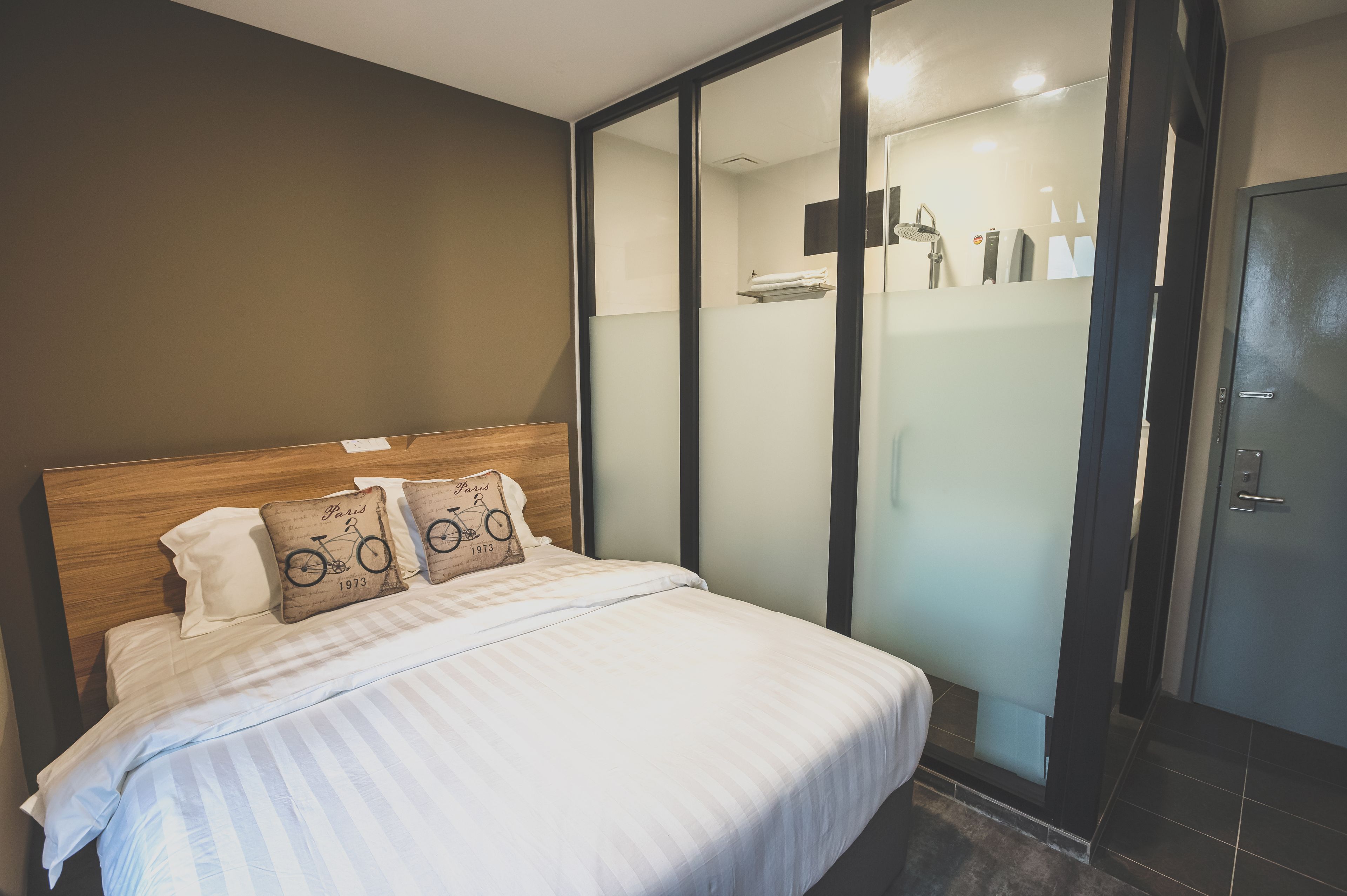 A hotel room with a bed, a wooden headboard, and a sliding glass door leading to a shower area.