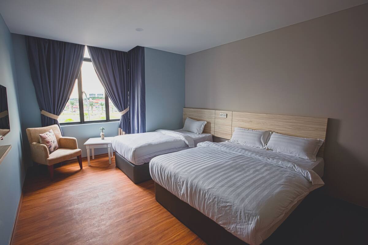 Une chambre d’hôtel avec deux lits, une chaise, une petite table et une fenêtre avec des rideaux.