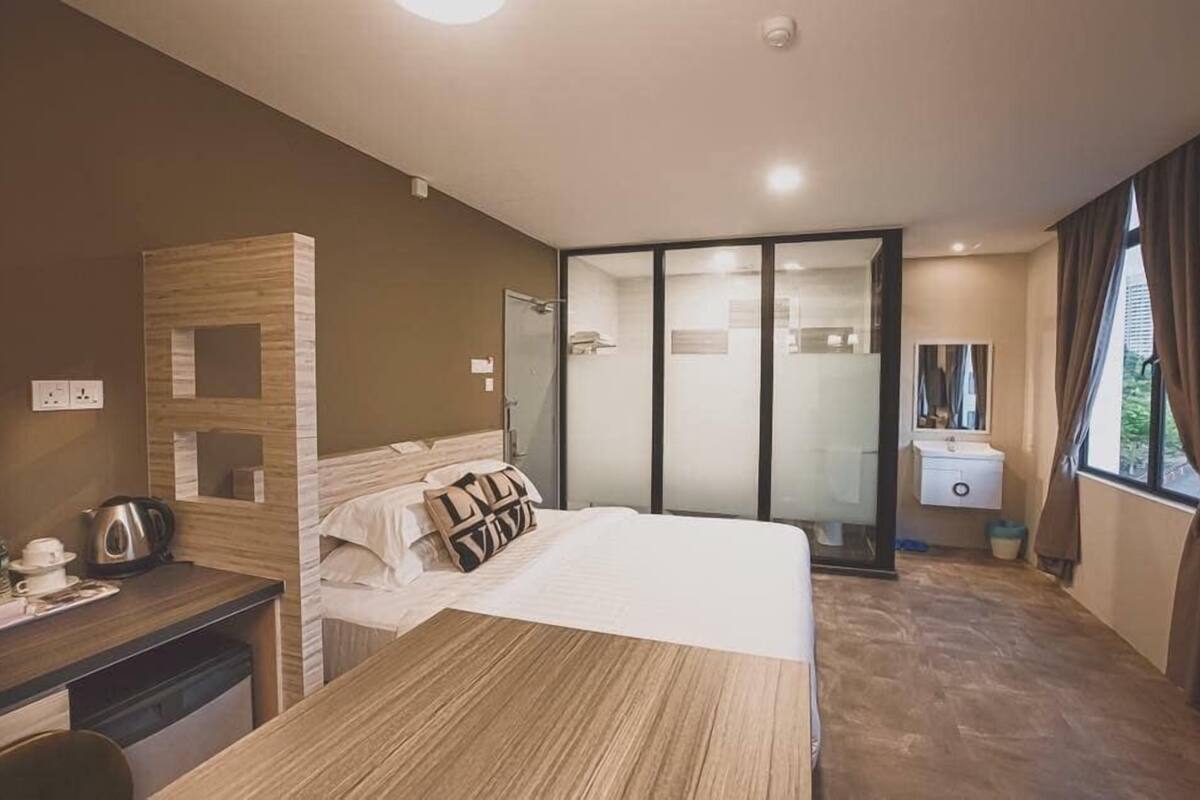 Une chambre d’hôtel moderne dotée d’un grand lit, d’un bureau avec une bouilloire, d’un miroir et d’une porte-fenêtre coulissante donnant sur la salle de bain.
