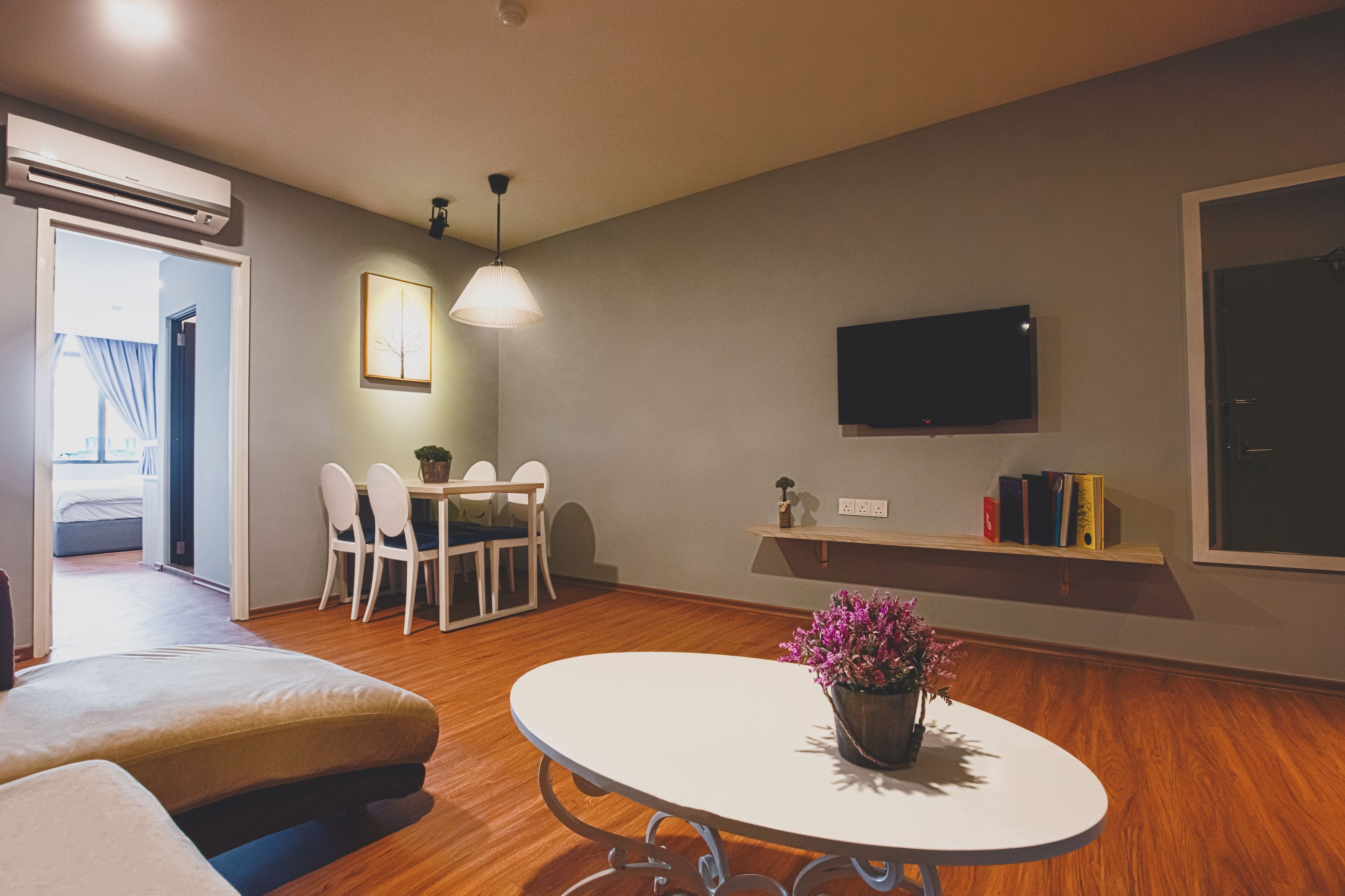 A modern living room with a round table, a sofa, a dining area with chairs, a TV mounted on the wall, and a bookshelf.