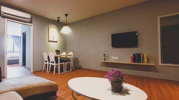A modern living room with a round table, a sofa, a dining area with chairs, a TV mounted on the wall, and a bookshelf.