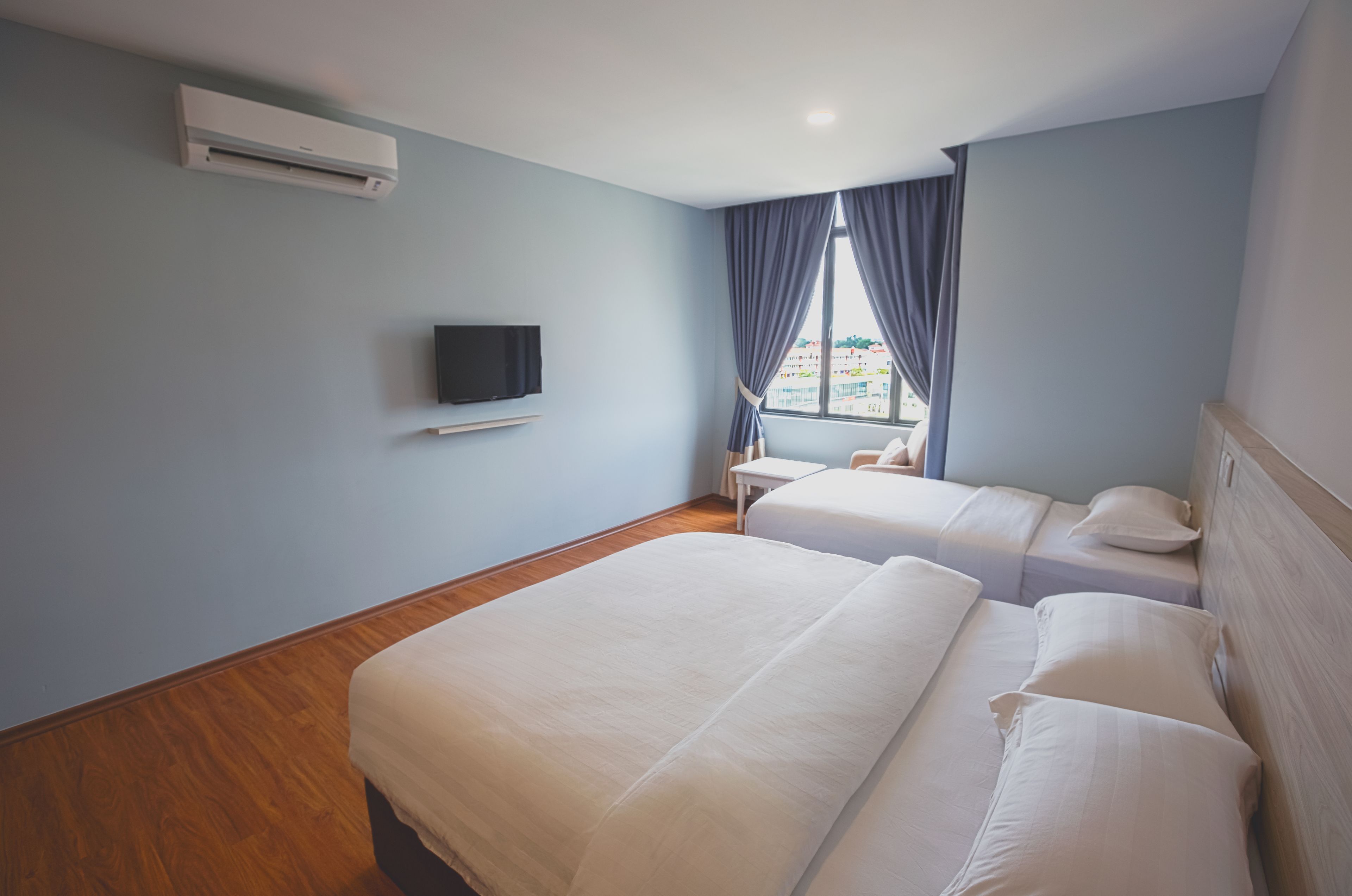 A hotel room with two beds, a flat-screen TV, a window with curtains, and an air conditioning unit.