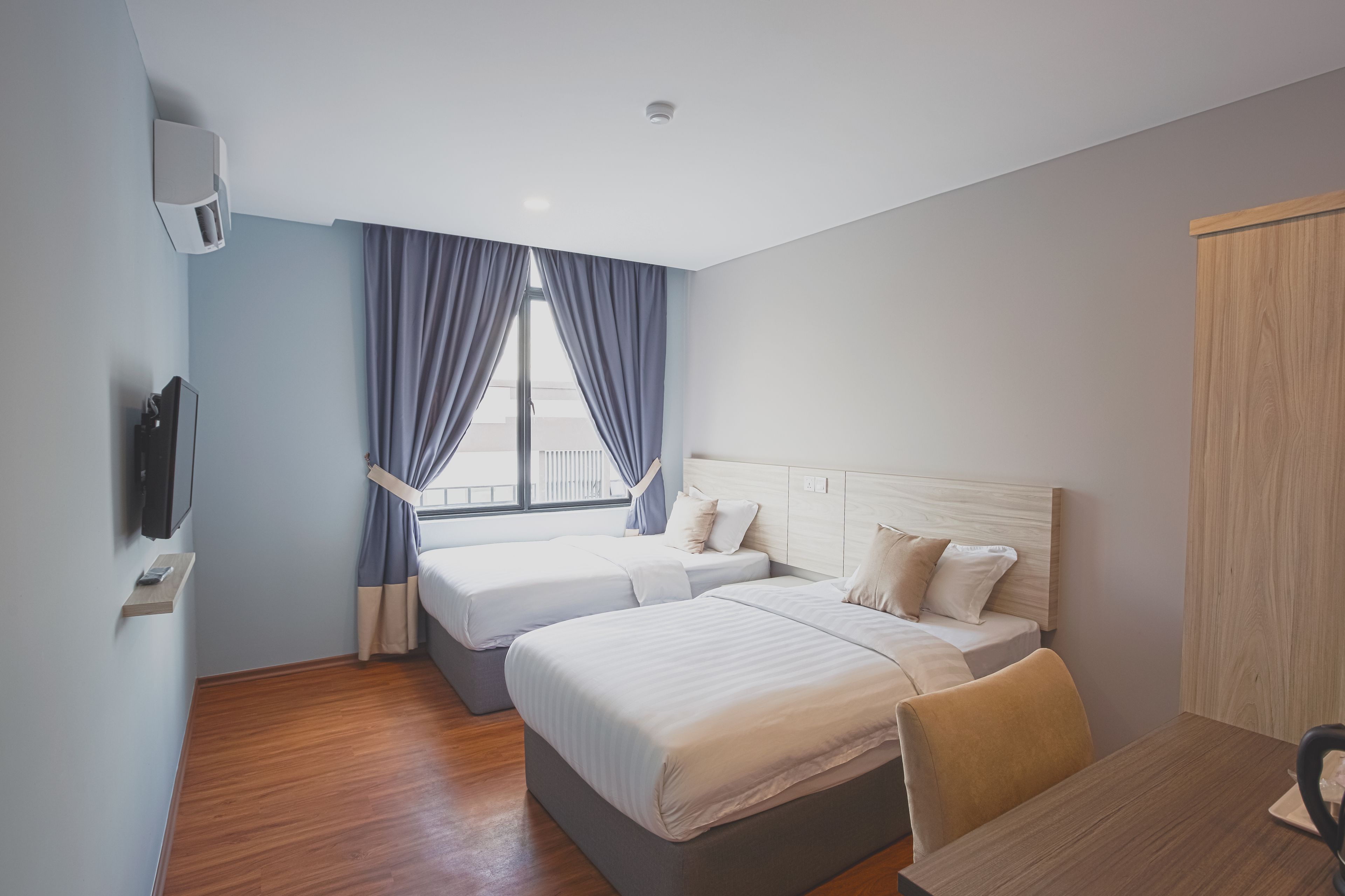 A hotel room with two beds, a wooden desk, a TV, and a window with curtains.