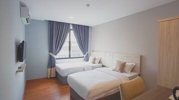 A hotel room with two beds, a wooden desk, a TV, and a window with curtains.