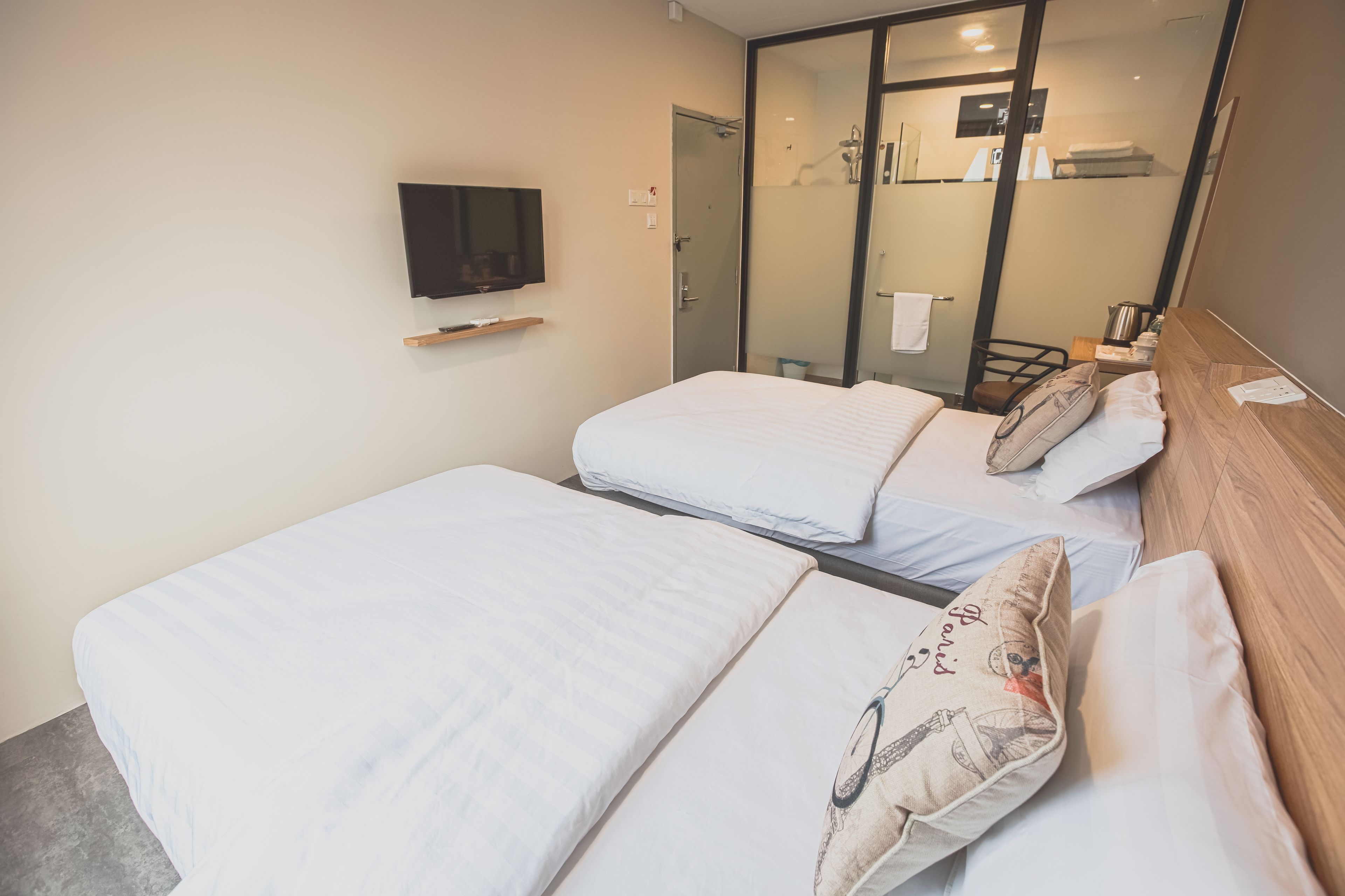 A hotel room with two beds, a TV on the wall, and a sliding door leading to a bathroom.