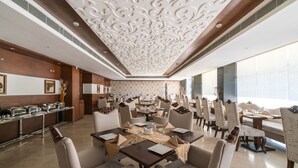 A spacious dining area with high-backed chairs, a central table with a placemat, and a decorative ceiling. - Hotel LN Courtyard (Ajmer)