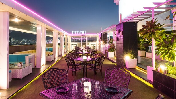 An outdoor dining area with tables and chairs, a pool, and a view of the city at night. - Hotel LN Courtyard (Ajmer)