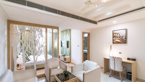 A modern living room with a sofa, chairs, a coffee table, and a desk. There is a large window with a view of greenery outside. - Hotel LN Courtyard (Ajmer)