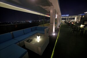 Una terrazza sul tetto con un divano blu, un tavolo con piano in vetro e luce, e vista sulla città di notte.