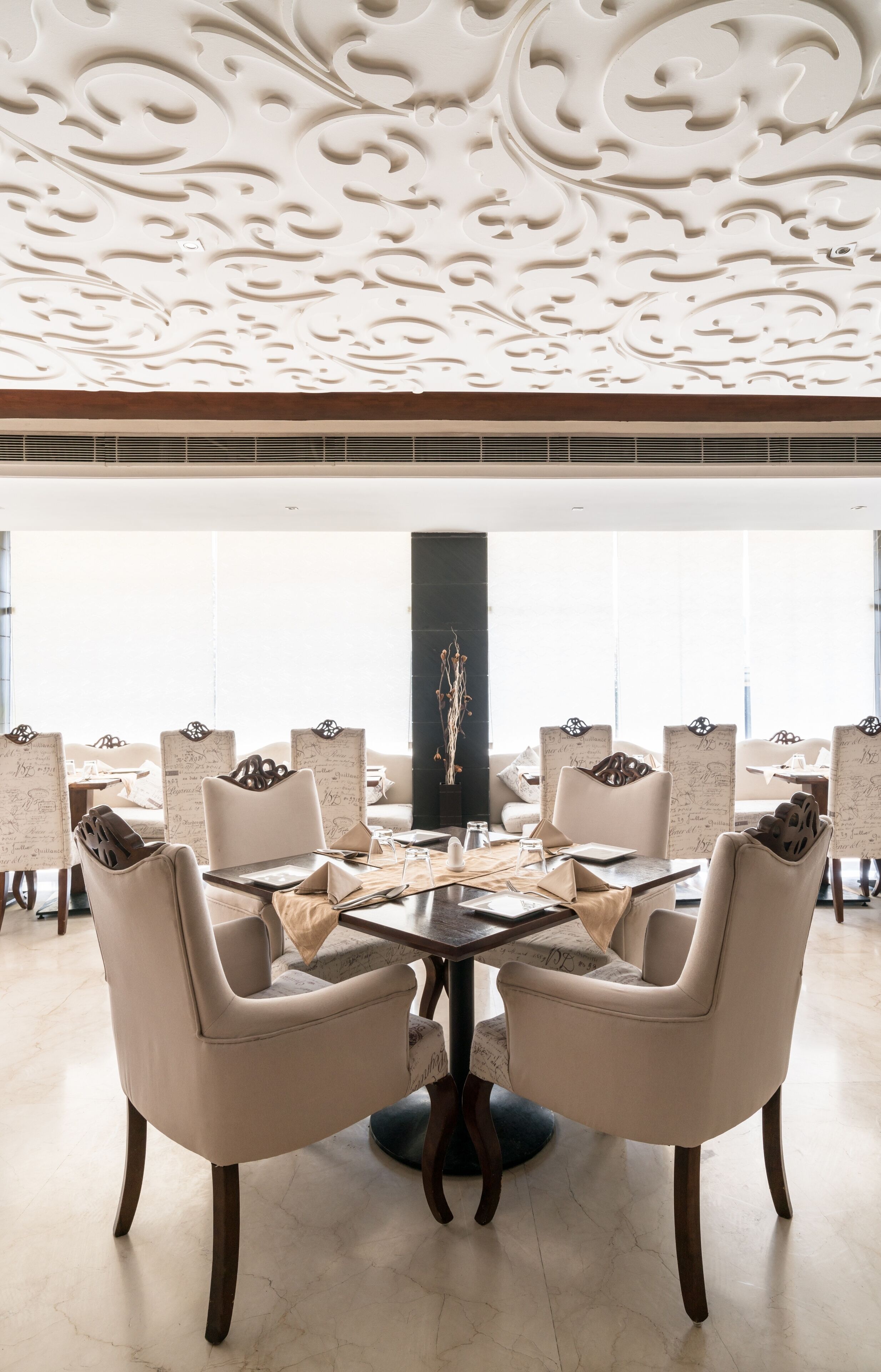 A dining area with a round table, six upholstered chairs, and a decorative ceiling.