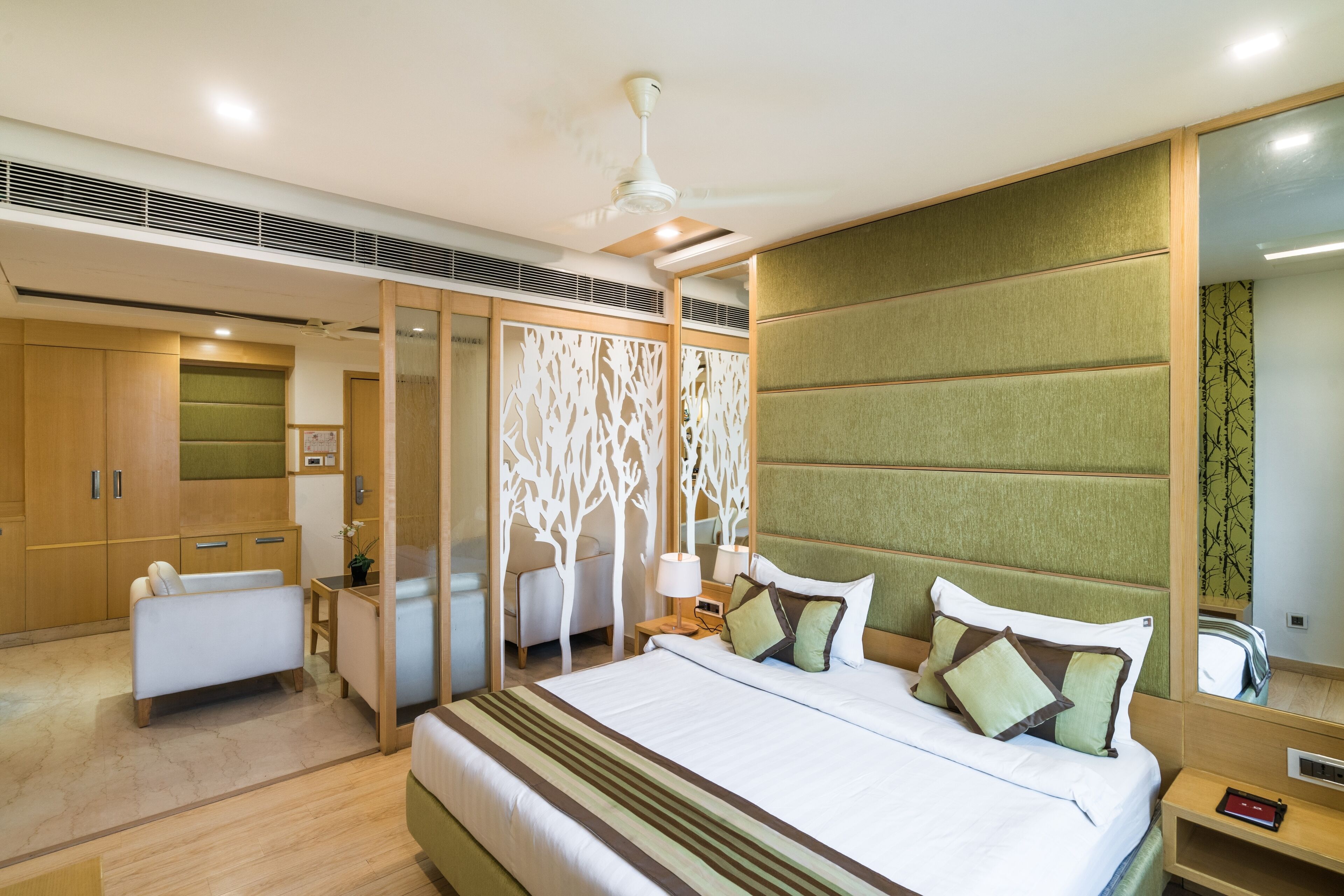 A modern hotel room with a large bed, a separate seating area, a vanity, and a large mirror.