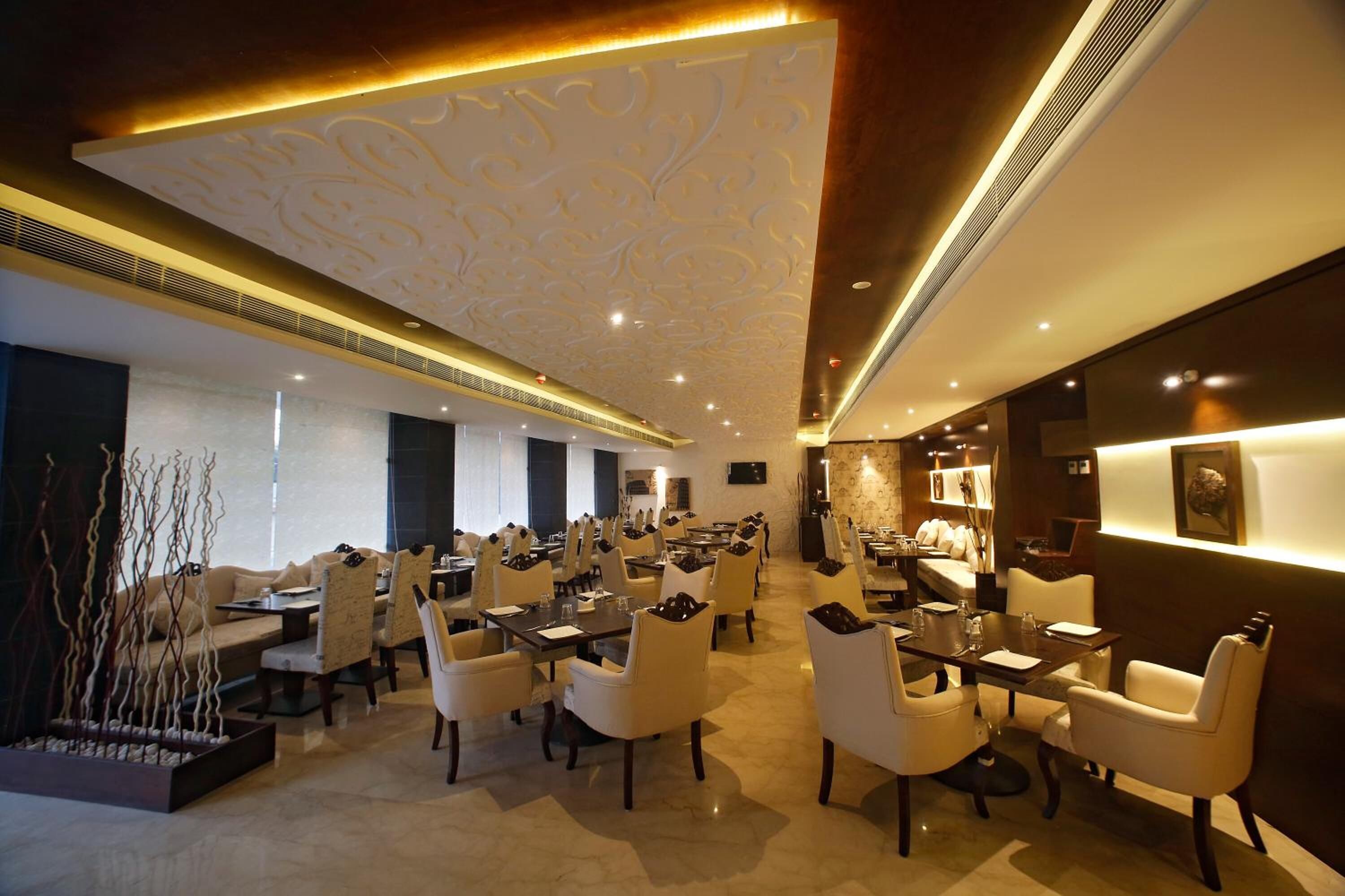 Un vaste espace de restauration d’hôtel, doté de nombreuses tables et chaises, d’un plafond décoratif et d’un aménagement intérieur moderne.