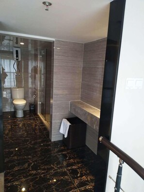 A modern bathroom with a glass shower enclosure, a toilet, and a vanity with a towel hanging. - Home Plus Suite Hotel And Apartment (Wuhan)