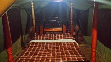 Una cama individual con estructura de madera y colcha de cuadros en una habitación tipo tienda de campaña.