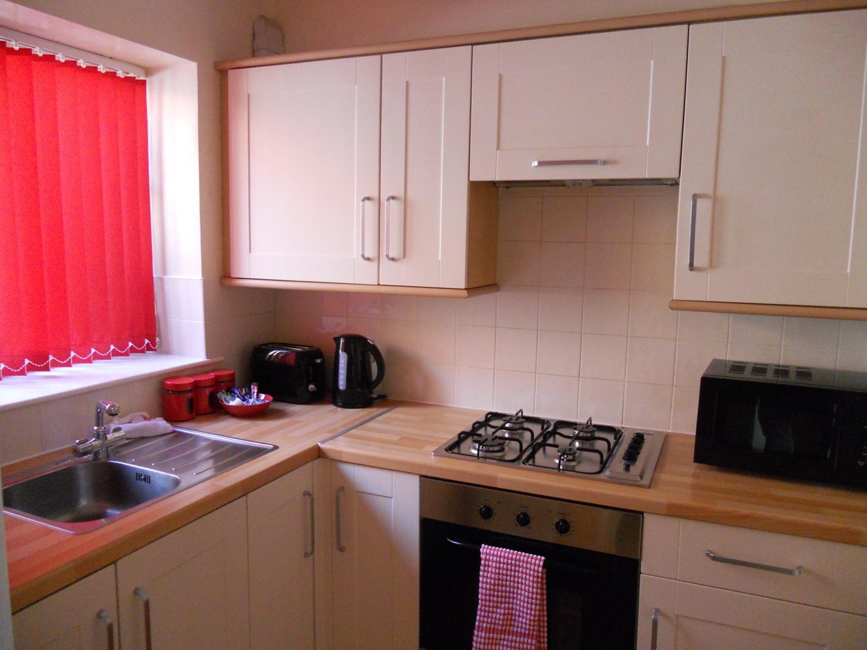 A kitchen with white cabinets, a gas stove, a sink, a toaster, and a kettle.