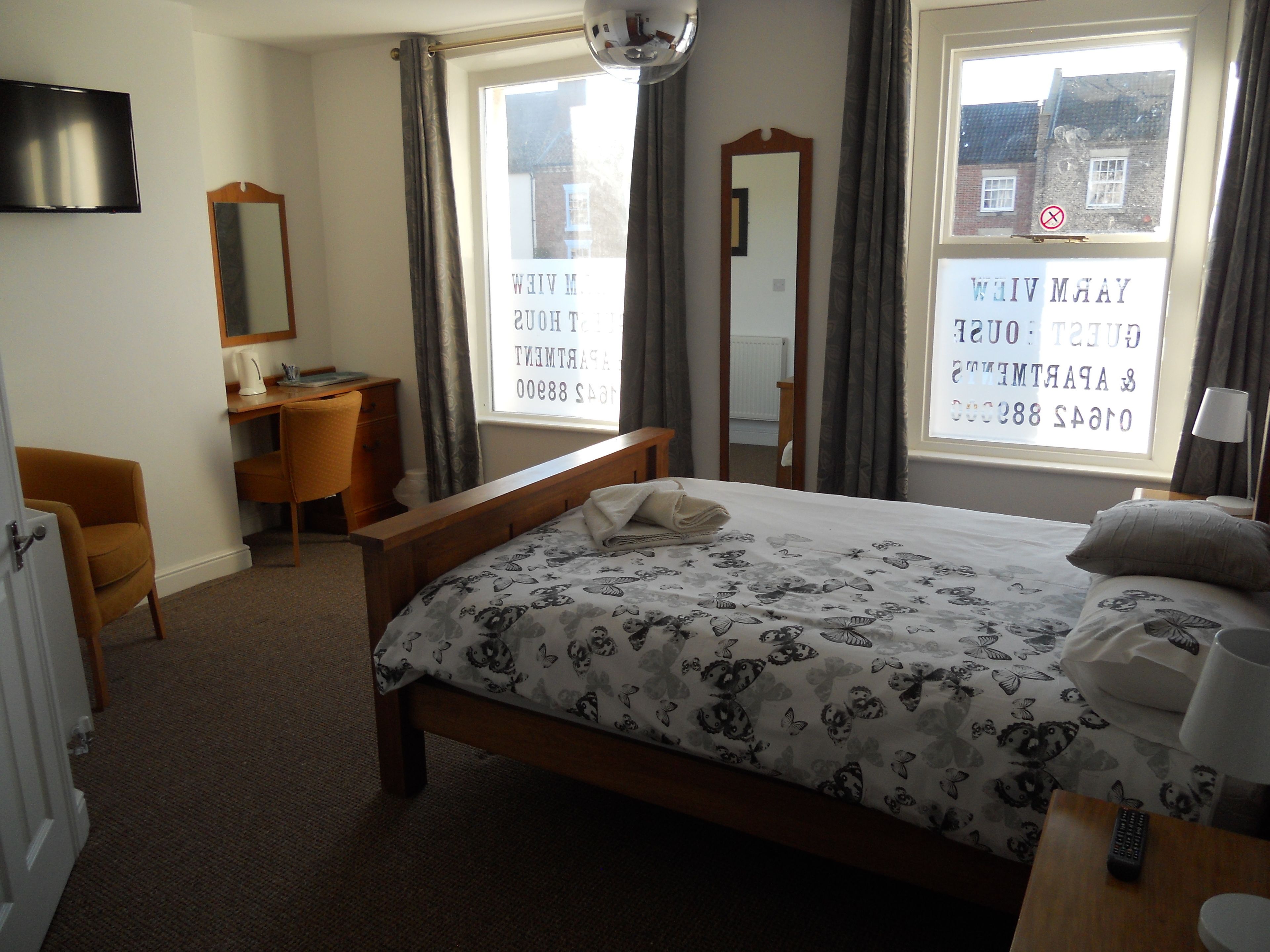 A hotel room with a bed, a desk, a chair, a mirror, and a television.