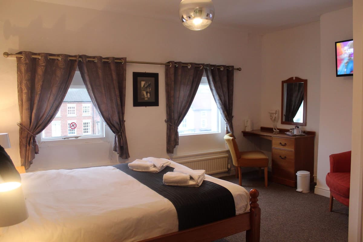 A hotel room with a bed, a desk, a chair, a television, and a window with curtains.