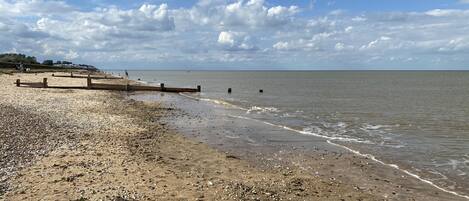A beach with pebbles and shells, a wooden walkway, and a calm sea under a partly cloudy sky.