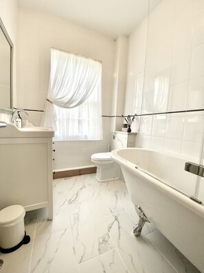 A modern bathroom with a freestanding bathtub, a toilet, and a sink. - Green Cottages (Sittingbourne)