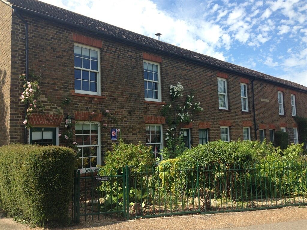 A brick building with multiple windows and a green fence in front.