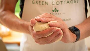 A person wearing a white apron with "GREEN COTTAGES Kitchen" printed on it, holding a piece of dough.