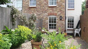 A brick house with a garden, a wooden fence, and a bench. - Green Cottages (Sittingbourne)