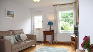 A living room with a sofa, a lamp, a TV, a window with curtains, and a plant. - Green Cottages (Sittingbourne)