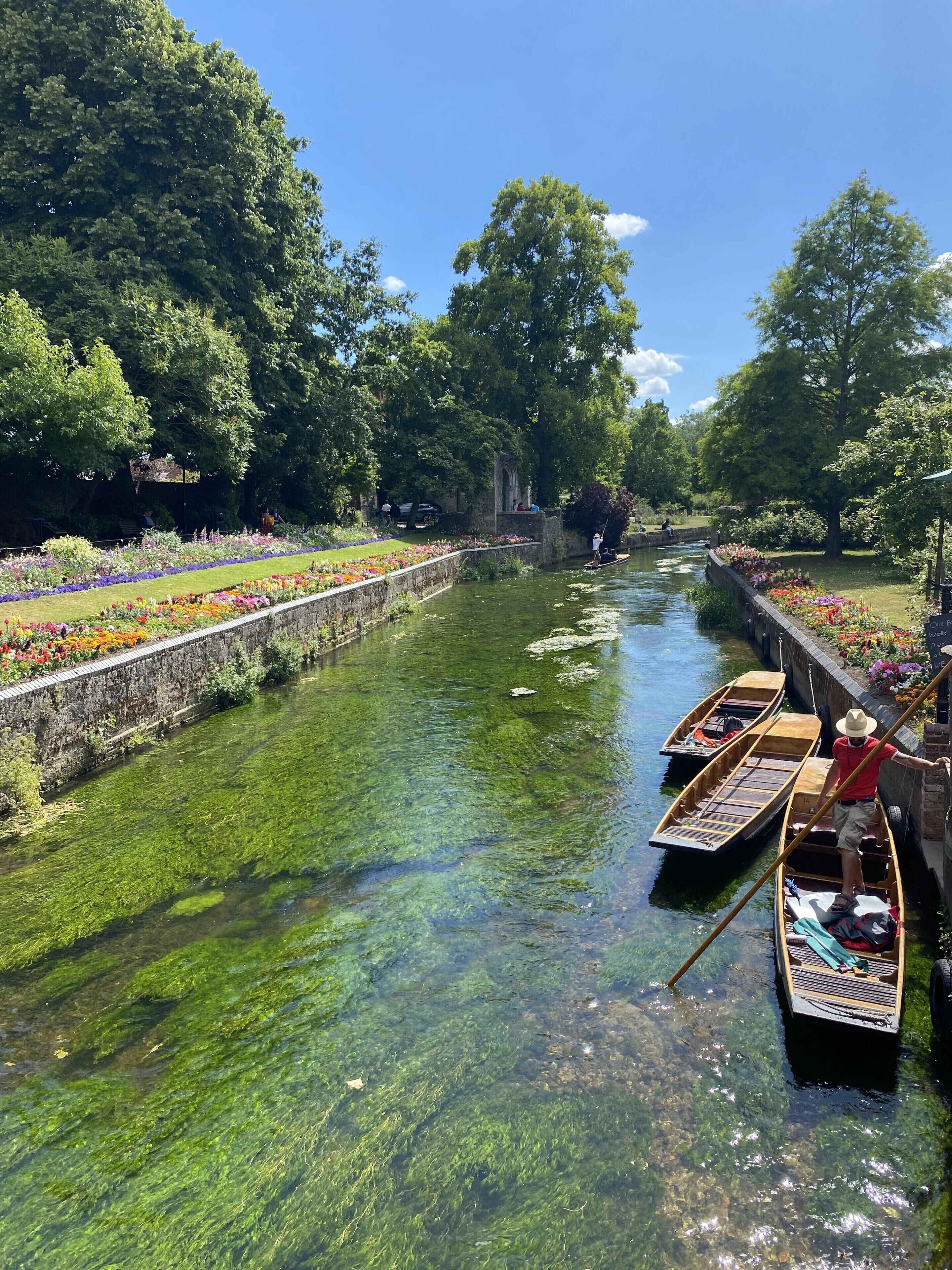 Un canal con barcos, rodeado de abundante vegetación y macizos de flores.