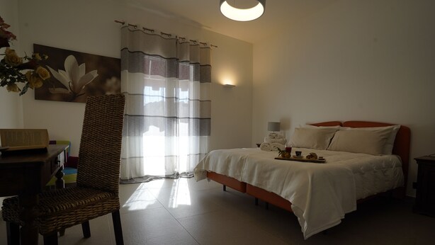 Un dormitorio con cama, una silla, una mesa y una ventana con cortinas.