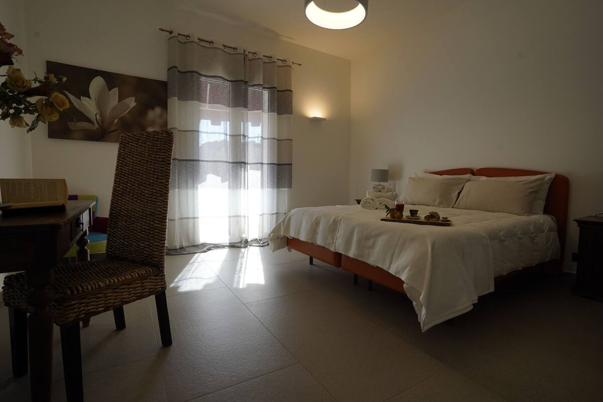 Une chambre à coucher avec un lit, une chaise, une table et une fenêtre avec des rideaux.