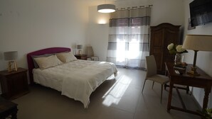 Un dormitorio con cama, mesitas de noche, una silla, escritorio, lámpara, armario y televisor en la pared.