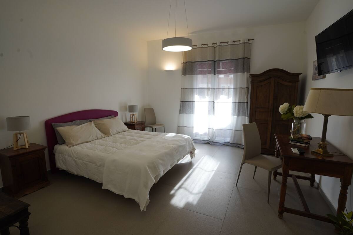 Une chambre à coucher avec un lit, des tables de chevet, une chaise, un bureau, une lampe, une armoire et un téléviseur fixé au mur.