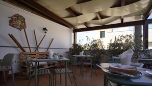 Un área de comedor al aire libre con muebles de madera rústica y sillas de metal, una mesa con un pastel y vistas a un edificio a través de la ventana.