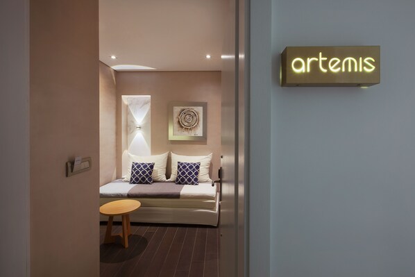 A modern hotel room with a bed, a small table, a wall-mounted sign, and a decorative wall piece.