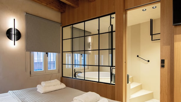 A hotel room with a large window, a bathtub, and a wooden staircase. - Consolato Boutique (Chania)