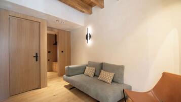 Una sala de estar moderna con un sofá gris, un sillón de cuero marrón, piso de madera y techo de madera.