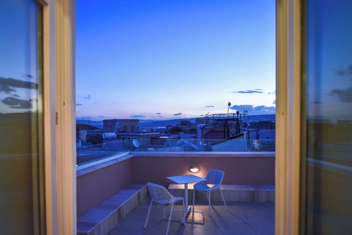 A rooftop terrace with a table and chairs, a view of the cityscape, and a glass railing.