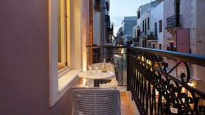 A balcony with a table and chairs, overlooking a street with buildings. - Consolato Boutique (Chania)