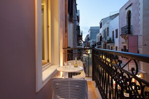 A balcony with a table and chairs, overlooking a street with buildings.