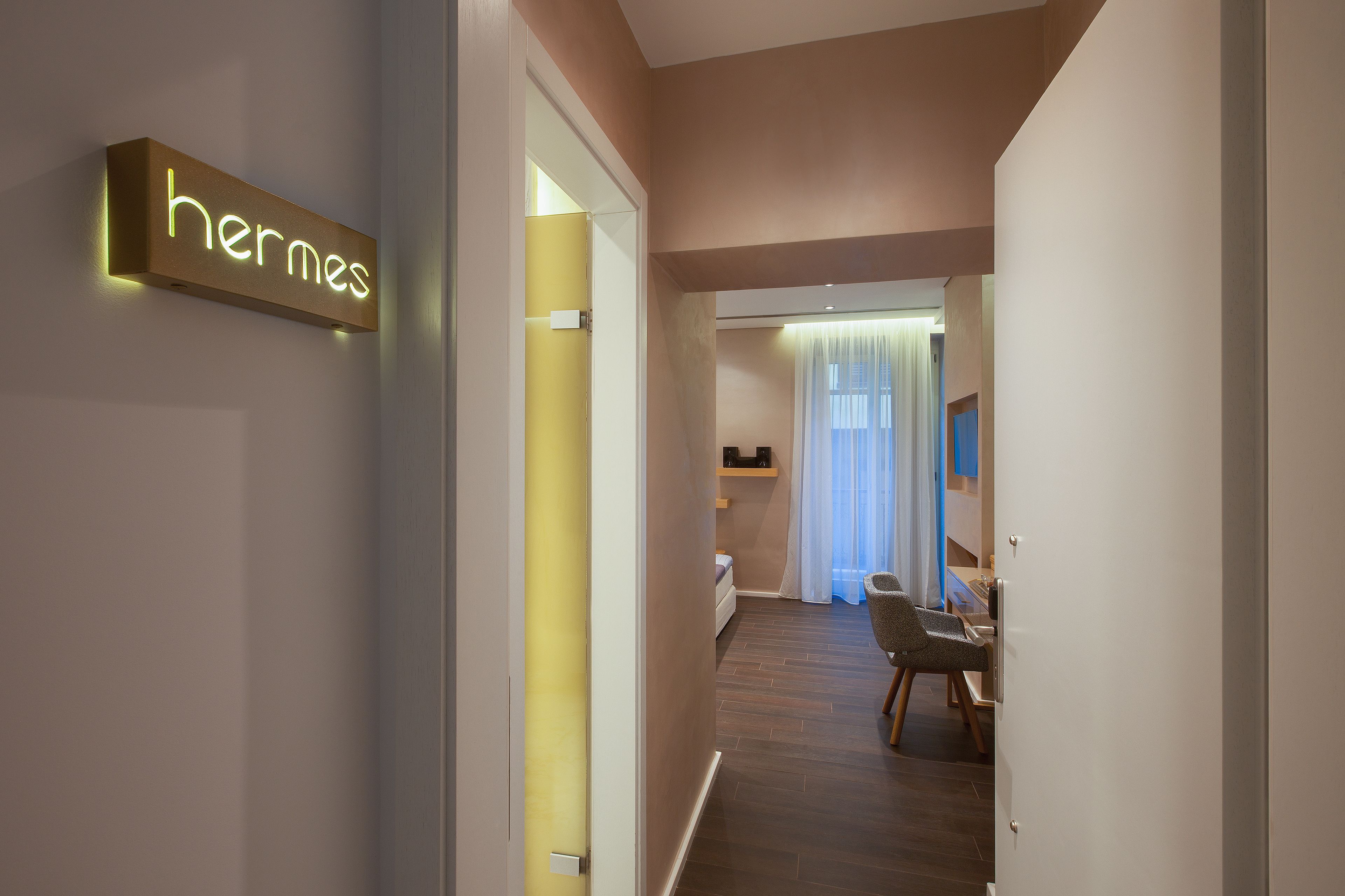 A hallway with a sign reading "hermes" and a glimpse of a room with a bed and a chair.