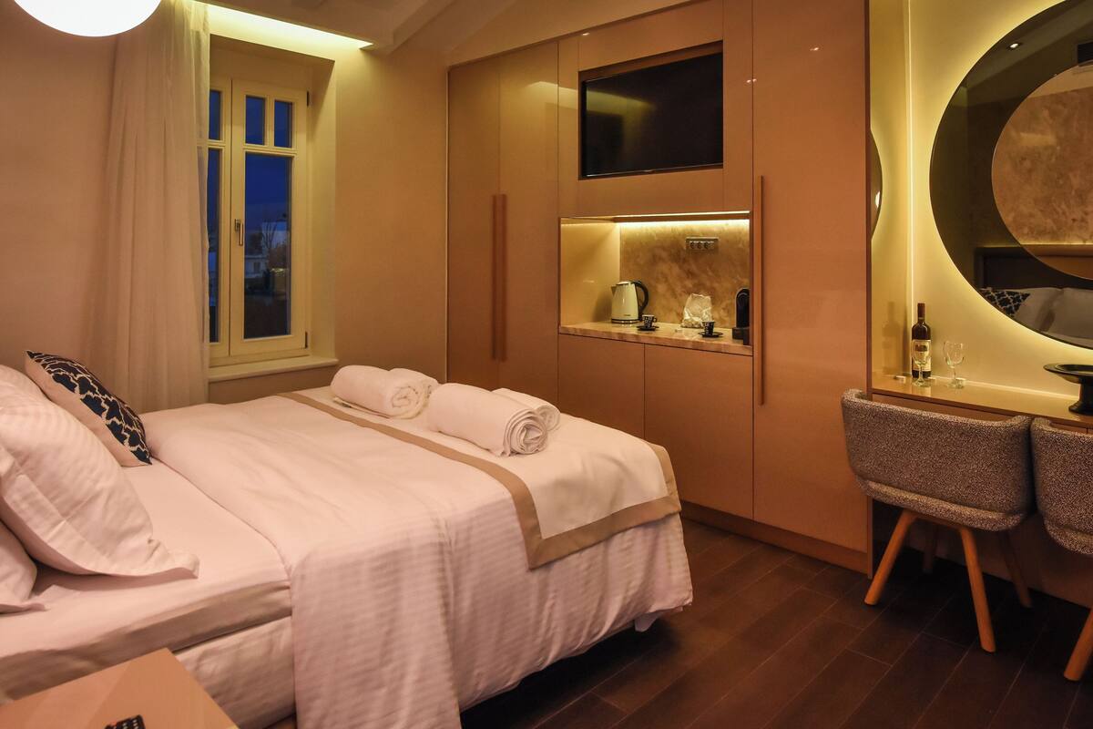A hotel room with a bed, a desk, a chair, a mirror, and a window.