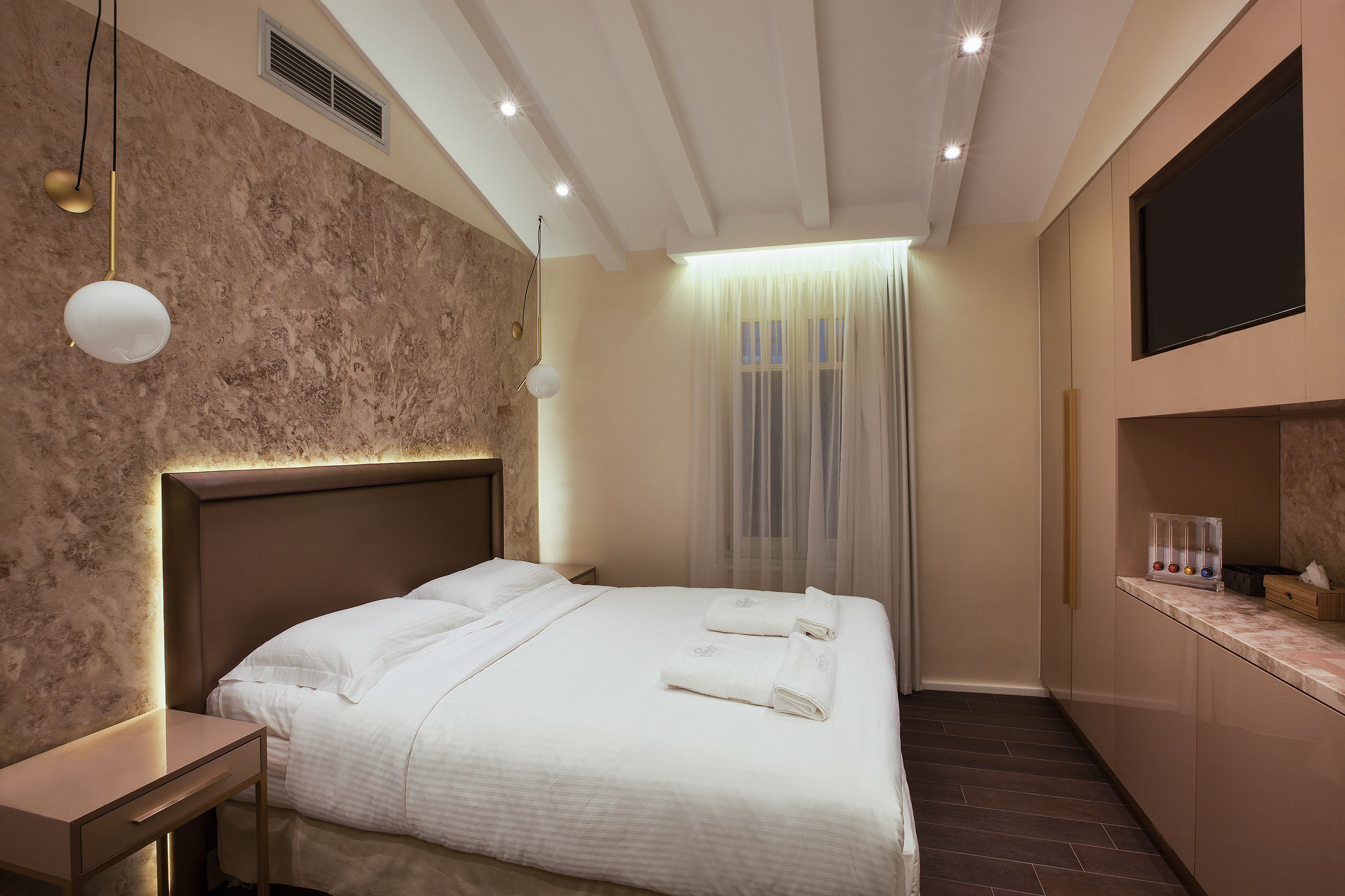 Una habitación de hotel moderna con una cama grande, una mesita de noche y un televisor integrado.