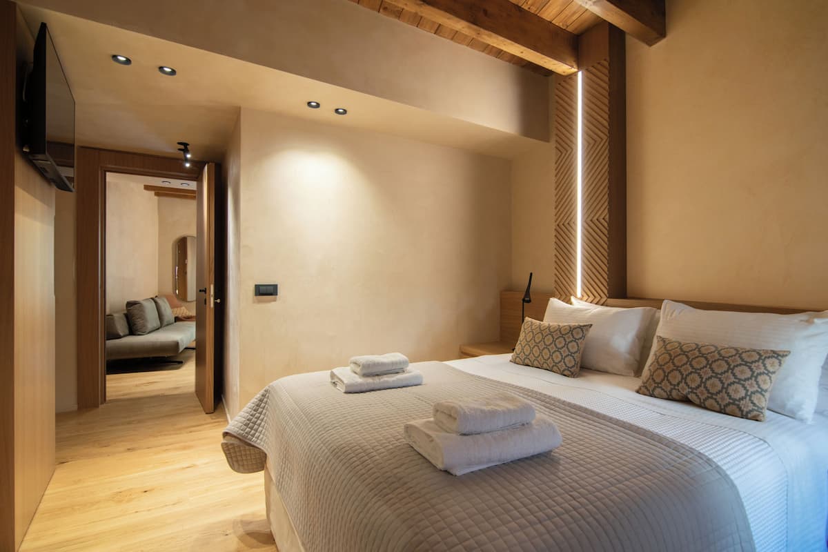 A hotel room with a large bed, a flat-screen TV mounted on the wall, and a wooden ceiling.