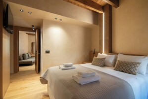 A hotel room with a large bed, a flat-screen TV mounted on the wall, and a wooden ceiling.