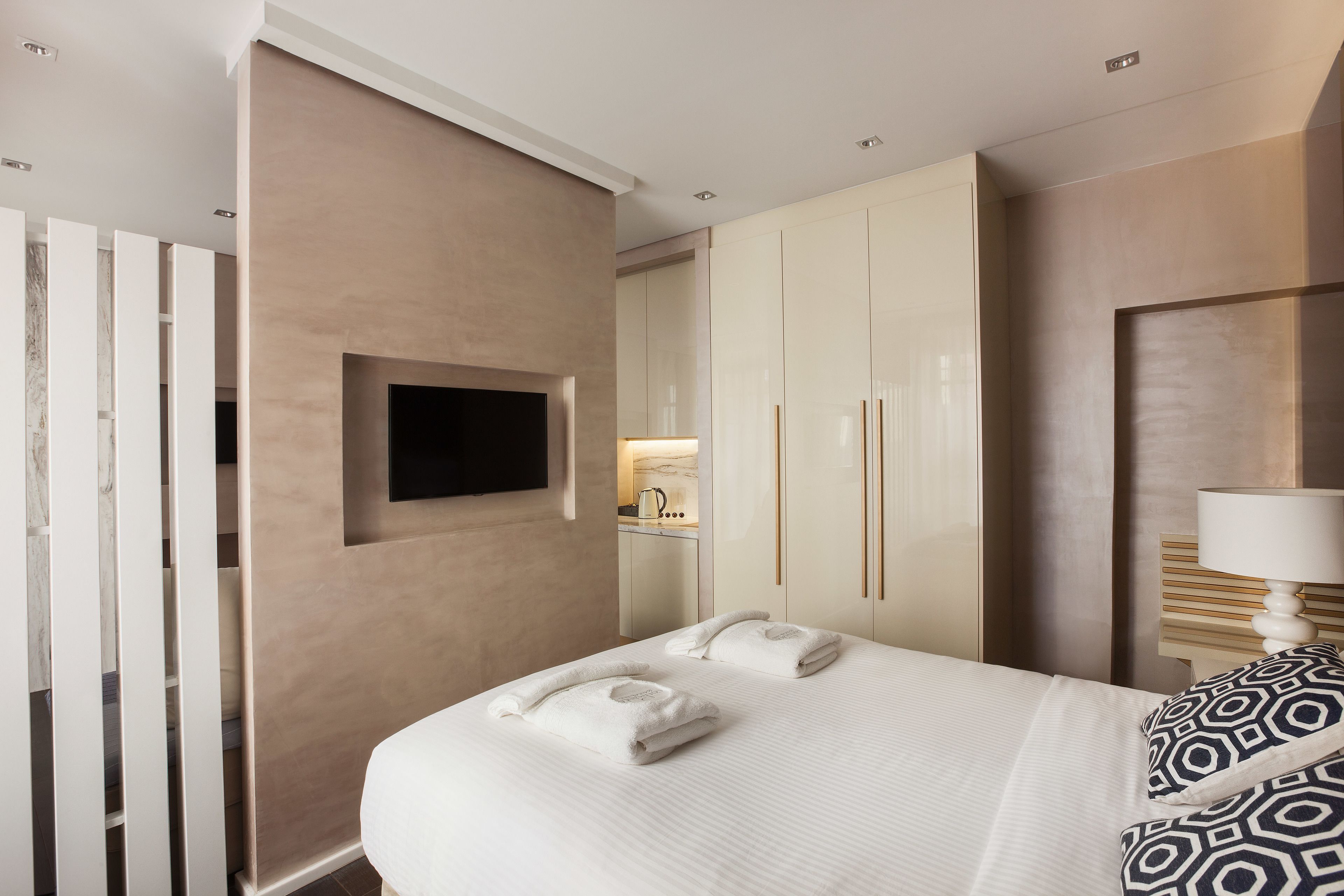 A hotel room with a bed, a TV mounted on the wall, a wardrobe, and a bedside table with a lamp.