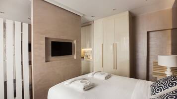 A hotel room with a bed, a TV mounted on the wall, a wardrobe, and a bedside table with a lamp.