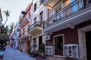 Une rue étroite bordée de bâtiments aux couleurs vives, dont certains sont dotés de balcons et de plantes en pot.