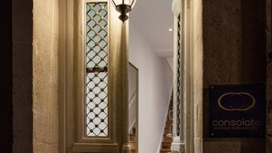 A narrow hallway with a decorative door, a lit wall-mounted lamp, and a sign for 'Consolato Boutique Suites & Bungalows'. - Consolato Boutique (Chania)