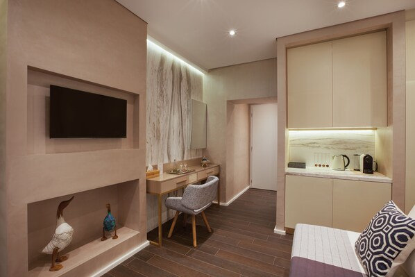Une chambre d’hôtel moderne dotée d’une télévision  à écran plat, d’un bureau avec une chaise, d’un coin cuisine intégré et d’un lit agrémenté d’oreillers à motifs.